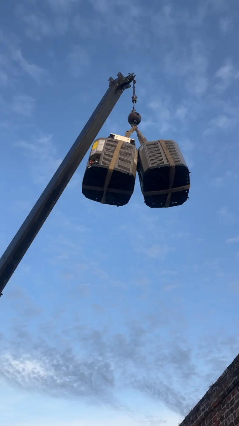 Two rooftop HVAC units lifted by a crane against a blue sky, New Orleans
